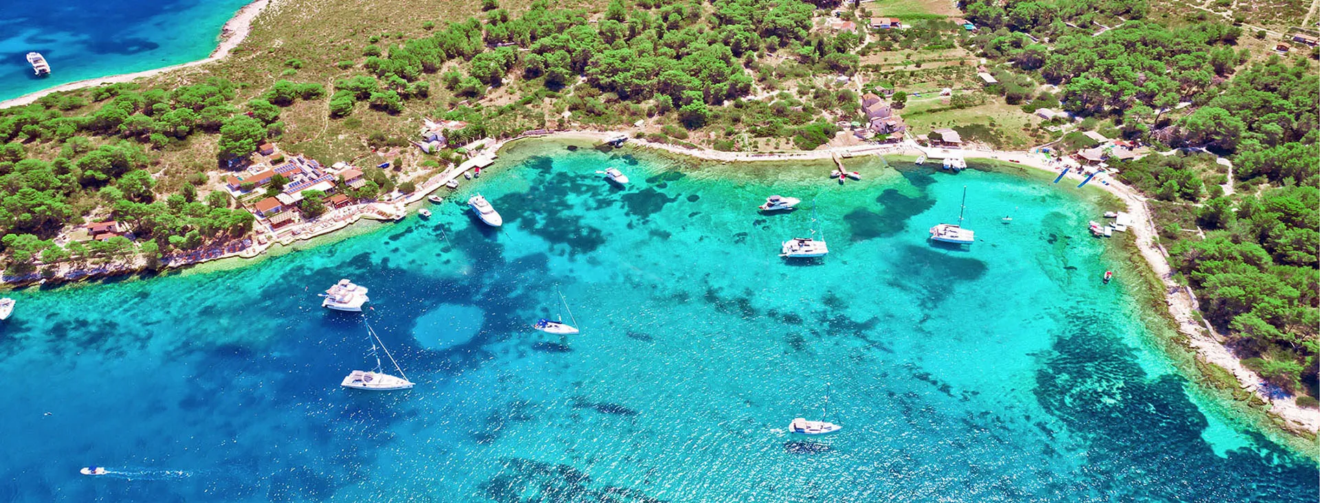 Veduta aerea di una baia cristallina con barche a vela tra le isole della Dalmazia