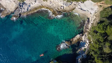 Vista aerea della Baia di Pola, una barca rossa che naviga nella baia con acque cristalline e costa rocciosa
