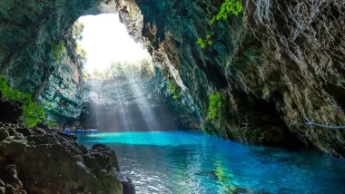 I raggi solari filtrano nella Grotta Melissani a Sami, Cefalonia, illuminando le acque turchesi sotterranee.