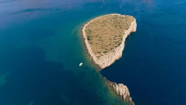 Isolotto Piskera Isole Incoronate - Vista dall'alto ha la forma di cuore,si vede una barca a vela che si distacca sullo sfondo blu profondo del mare.
