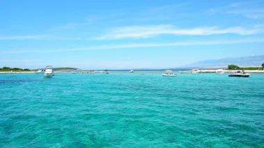 Immagine di barche a vela e motore tra le acque limpide di una delle baie di Lussino con una vista sulle colline istriane in lontananza.