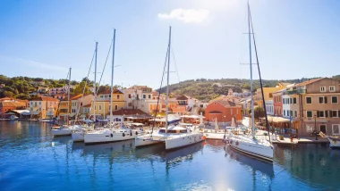 Vele alzate e barche ormeggiate nel pittoresco porto di Gaios a Paxos, con le classiche case color pastello in sfondo.