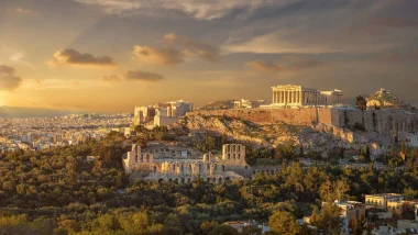 L'Acropoli di Atene che illumina la città con la sua storia al tramonto, con il Partenone e il Teatro di Dioniso che emergono su un sfondo di montagne e cielo pastello.