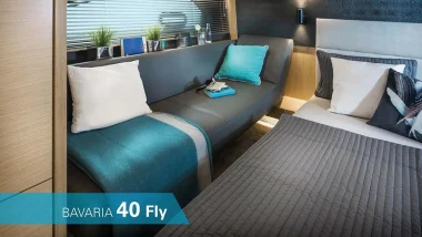 Accogliente cabina del Bavaria 40 Fly con un letto matrimoniale e un divano, arredata con cuscini color turchese e dettagli moderni.